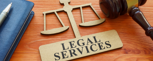 A brown desk in the office of a personal injury solicitors. it has a book, pen, gavel and brass sign with legal services written on it.